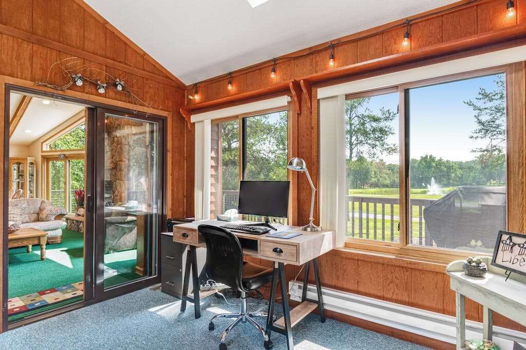 Una habitación con escritorio, ordenador y ventanas amplias.