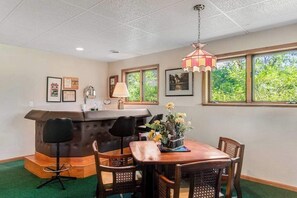 A dining area with a wooden table, four chairs, a bar area with a counter, and a hanging lamp. - Golf course-front home with 2 pools, private beach, boat launches, tennis, grill (Nekoosa)