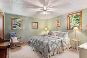 A bedroom with a bed, a chair, a side table, a ceiling fan, and two windows.