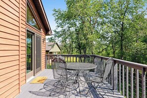 A wooden deck with a metal table and chairs, overlooking a wooded area. - Golf course-front home with 2 pools, private beach, boat launches, tennis, grill (Nekoosa)