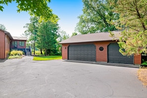 A residential driveway leading to a garage with a covered carport, surrounded by trees and a well-maintained lawn.