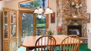 A dining area with a stone fireplace, a wooden dining table, and chairs. - Golf course-front home with 2 pools, private beach, boat launches, tennis, grill (Nekoosa)