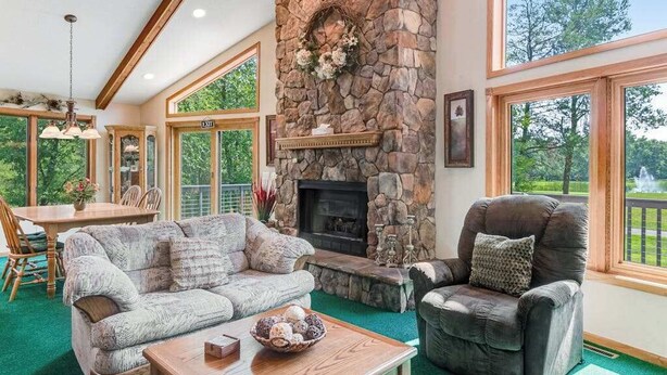 A cozy living room with a stone fireplace, a sofa, a chair, and a dining area with a table and chairs. - Golf course-front home with 2 pools, private beach, boat launches, tennis, grill (Nekoosa)