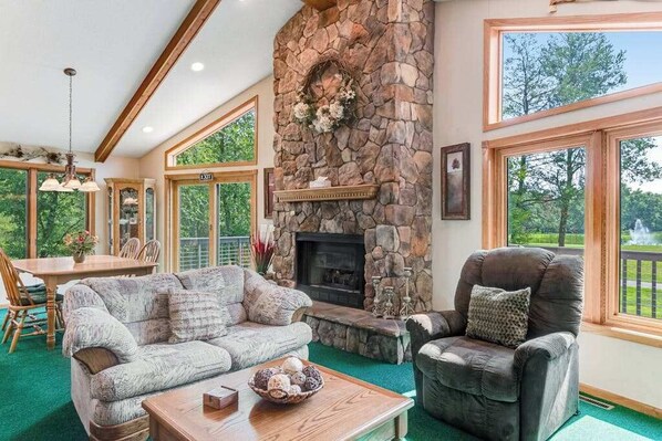 A cozy living room with a stone fireplace, a sofa, a chair, and a dining area with a table and chairs.