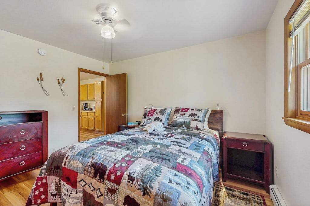 A bedroom with a quilted bedspread, a wooden dresser, a nightstand, and a ceiling fan.