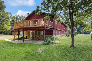 A two-story log cabin with a porch, stone foundation, and a well-maintained lawn. - Cozy wooded duplex w/ WiFi, full kitchen, shared W/D & near lakes & trails (Arkdale)