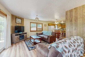 A living room with a television, sofa, coffee table, and a dining area with chairs and a table. - Cozy wooded duplex w/ WiFi, full kitchen, shared W/D & near lakes & trails (Arkdale)