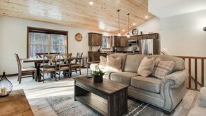 Un salon moderne avec un plafond en bois, un canapé, une table basse et un coin repas comprenant des chaises et une table.