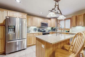 A kitchen with wooden cabinets, stainless steel appliances, a granite countertop island, and a hanging light fixture.