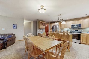 A dining area with a wooden table and chairs, a kitchen with wooden cabinets and appliances, and a sign on the wall.