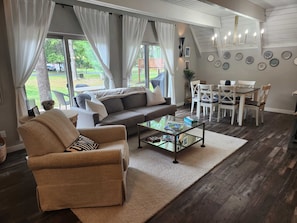 A living room with a sofa, armchair, coffee table, dining table with chairs, and a chandelier.