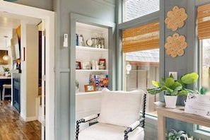 A room with a white armchair, a wooden floor, a bookshelf with various items, and a window with blinds. - Nekoosa Albatross A-Frame ‚Äì Lake Sherwood WI, Town of Rome, near Sand Valley. (Nekoosa)