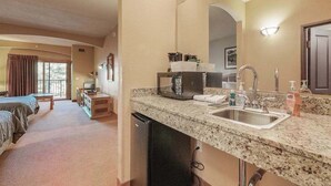 A hotel room with a kitchenette, a bed, a TV, and a view of the outdoors. - Lovely Studio + balcony + Perks (Wisconsin Dells)