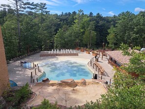 A pool area with lounge chairs, a hot tub, and a forested backdrop. - Spacious Condo Near Downtown Dells Attractions (Wisconsin Dells)