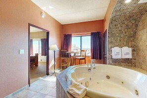 A hotel bathroom with a large bathtub, a dining area with a table and chairs, and a view through the window. - Spacious Condo Near Downtown Dells Attractions (Wisconsin Dells)
