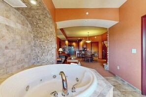 Ein geräumiges Badezimmer mit einer großen Badewanne, einem gefliesten Duschbereich und im Hintergrund ein sichtbarer Essbereich.