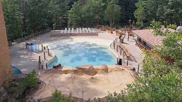 Eine Thermalquelle, umgeben von Liegestühlen und einem Pool, inmitten eines bewaldeten Geländes.