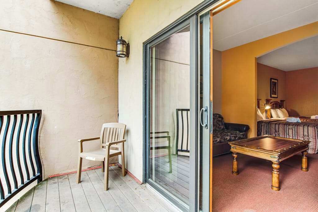 Uma varanda com cadeira, mesa e porta de vidro deslizante que dá para um quarto com cama e sofá.