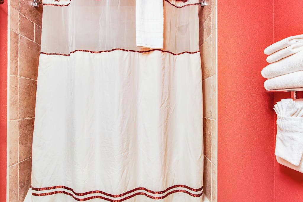 Un baño con cortina de ducha blanca, un perchero con toallas blancas y una pared roja.