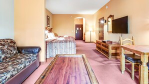 A hotel room with a bed, a sofa, a wooden table, a TV, and a desk with drawers. - Family Friendly Chula Vista Studio/Discount Perks (Wisconsin Dells)