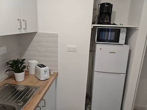 Eine kompakte Küche mit Mikrowelle, Toaster und Kaffeemaschine auf einem Regal.
