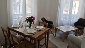 Een eetgedeelte met een houten tafel voor vier personen, twee stoelen, een klein bijzettafeltje en een potplant.