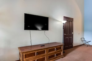 A room with a flat-screen TV mounted on the wall, a wooden dresser, a door, and a lamp. - Studio Escape at Chula Vista w/ Adventure Perk (Wisconsin Dells)