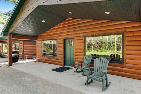 A log cabin with two rocking chairs outside, a covered patio, and a view of the surrounding forest. - Inviting Dog-Friendly Cabin with Hot Tub & AC (Conover)