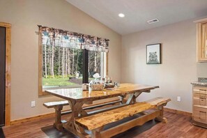A wooden dining table with benches, a window with a view of trees, and a framed picture on the wall. - Inviting Dog-Friendly Cabin with Hot Tub & AC (Conover)