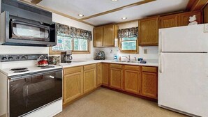 A kitchen with wooden cabinets, a microwave, stove, and refrigerator. - Dog-Friendly Retreat Near Trails & Lake with Full Kitchen, Central AC, & WiFi (Eagle River)