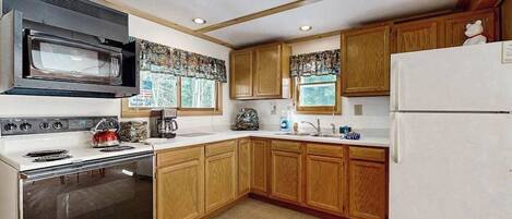 Una cocina con armarios de madera, microondas, estufa y refrigerador.