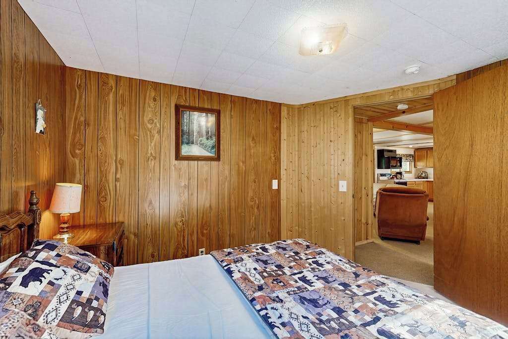 Une pièce aux murs en bois, un lit recouvert d’une couvre-lit à motifs, une table de chevet avec une lampe et un tableau encadré accroché au mur.