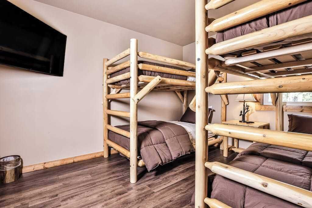 A bunk bed room with a wooden frame, a television mounted on the wall, and a window with a view.