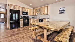 Une cuisine moderne avec des meubles de rangement en bois, un réfrigérateur noir, une table à manger en bois et un banc.