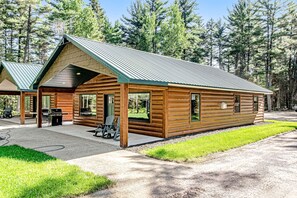 A log cabin with a metal roof, large windows, and a patio area with outdoor seating. - Stylish dog-friendly cabin w/hot tub, fireplace, patio, grill, central AC, & W/D (Conover)