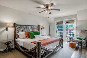 A bedroom with a wooden bed frame, a ceiling fan, a small round table, a chair, and a view through a door.