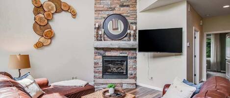 Un salon doté d’une cheminée, de canapés en cuir, d’une table basse et d’un téléviseur à écran plat fixé au mur.