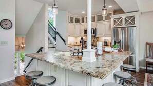 A kitchen with white cabinets, a granite countertop, and a stainless steel refrigerator. - Newly-built condo on Duck Lake with decks, private dock, & firepit (Eagle River)