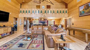 Interior d'una cabana de fusta amb un dormitori a l'altell, un saló amb sofà de cuir i una zona de menjador.