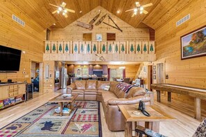 L’intérieur d’une cabane en rondins comprend une chambre à coucher située en mezzanine, un salon avec un canapé en cuir et un coin repas.