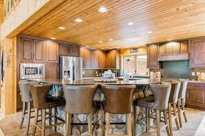 Une cuisine avec des meubles en bois, un îlot central doté de tabourets, un réfrigérateur en acier inoxydable et un four à micro-ondes.