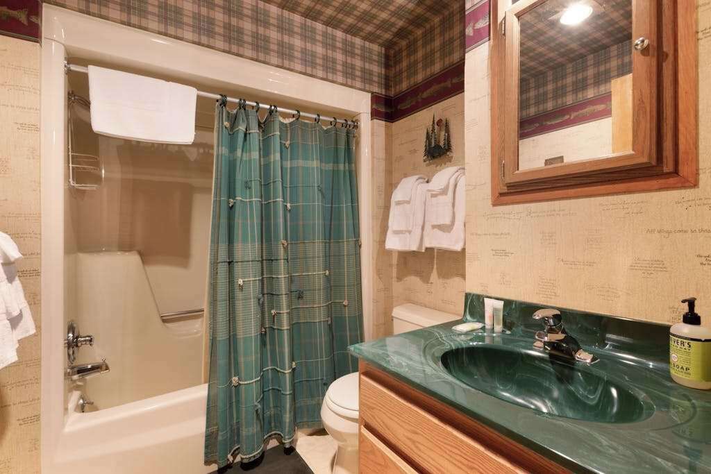A bathroom with a bathtub, a shower curtain, a toilet, a sink with a mirror, and a towel rack.