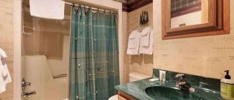 A bathroom with a bathtub, a shower curtain, a toilet, a sink with a mirror, and a towel rack.
