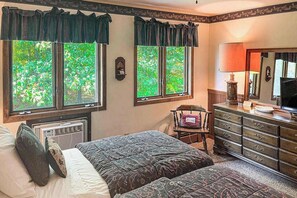 A bedroom with two beds, a dresser, a chair, and a large window with a view of trees.