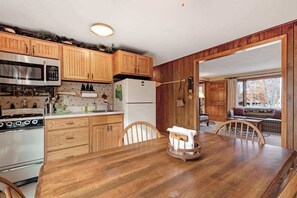A kitchen with wooden cabinets, a microwave, stove, and refrigerator. There is a dining table with chairs and a window with a view.