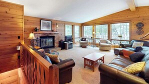 Un intérieur de chalet chaleureux avec une cheminée, des canapés en cuir et de grandes fenêtres.