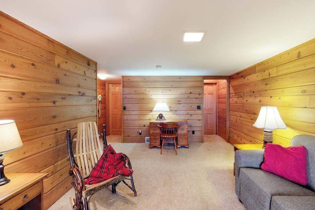 Une pièce aux murs en bois, avec une chaise, un canapé, une table et des lampes.