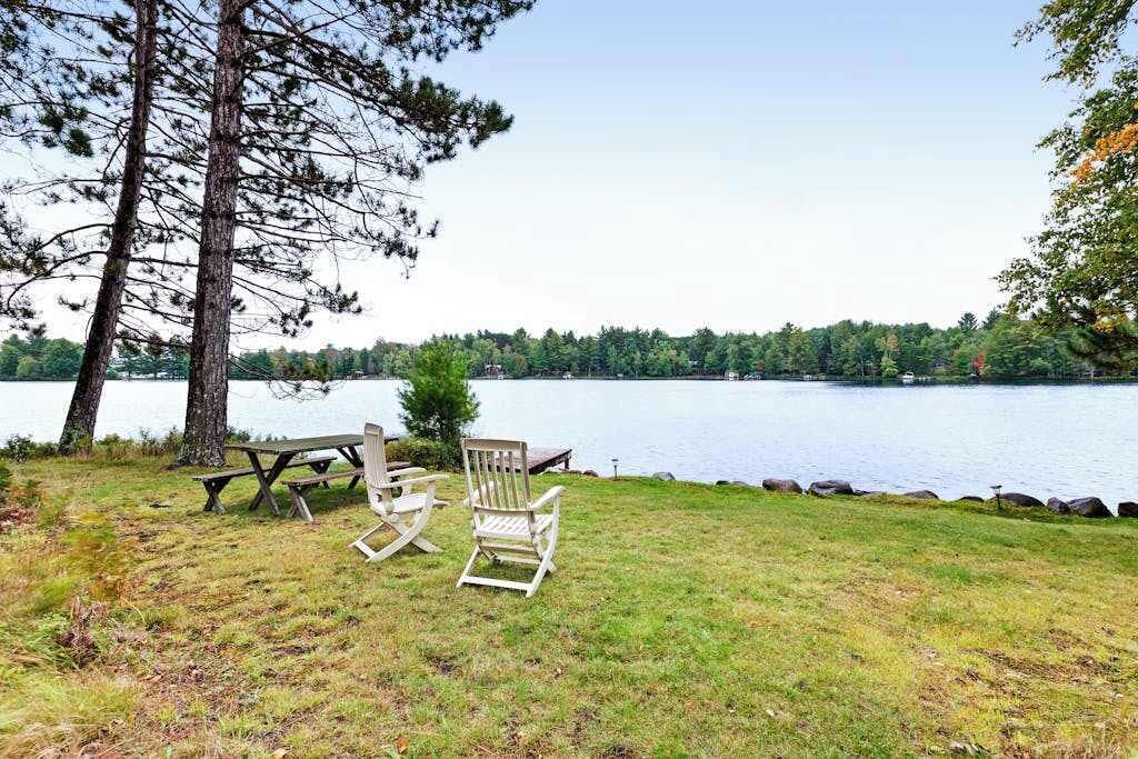 A lakeside setting with a picnic table and Adirondack chairs.