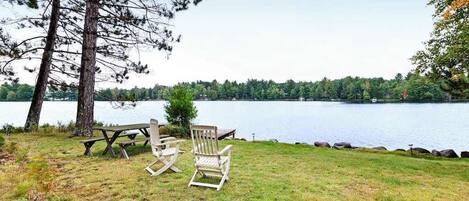 A lakeside setting with a picnic table and Adirondack chairs.