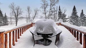 Un espacio al aire libre cubierto de nieve con una barandilla de madera y una silla también cubierta de nieve.